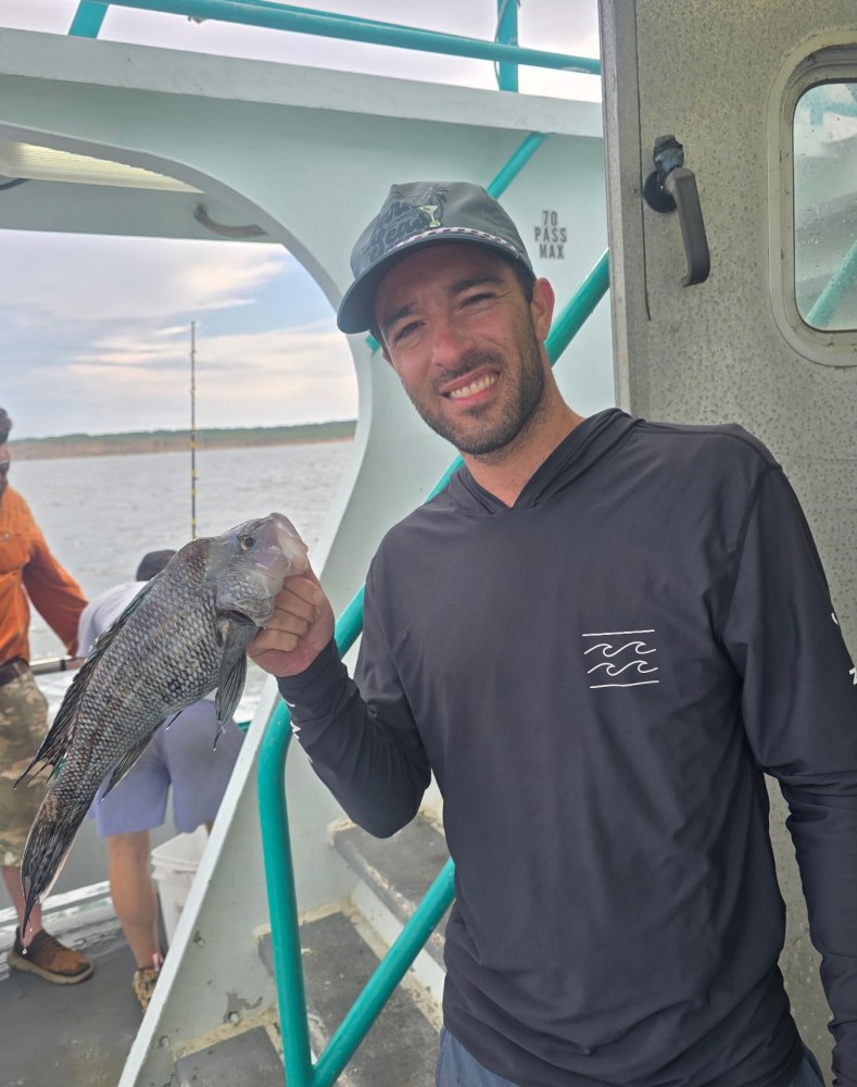 Man smiling and holding a fish on a boat.