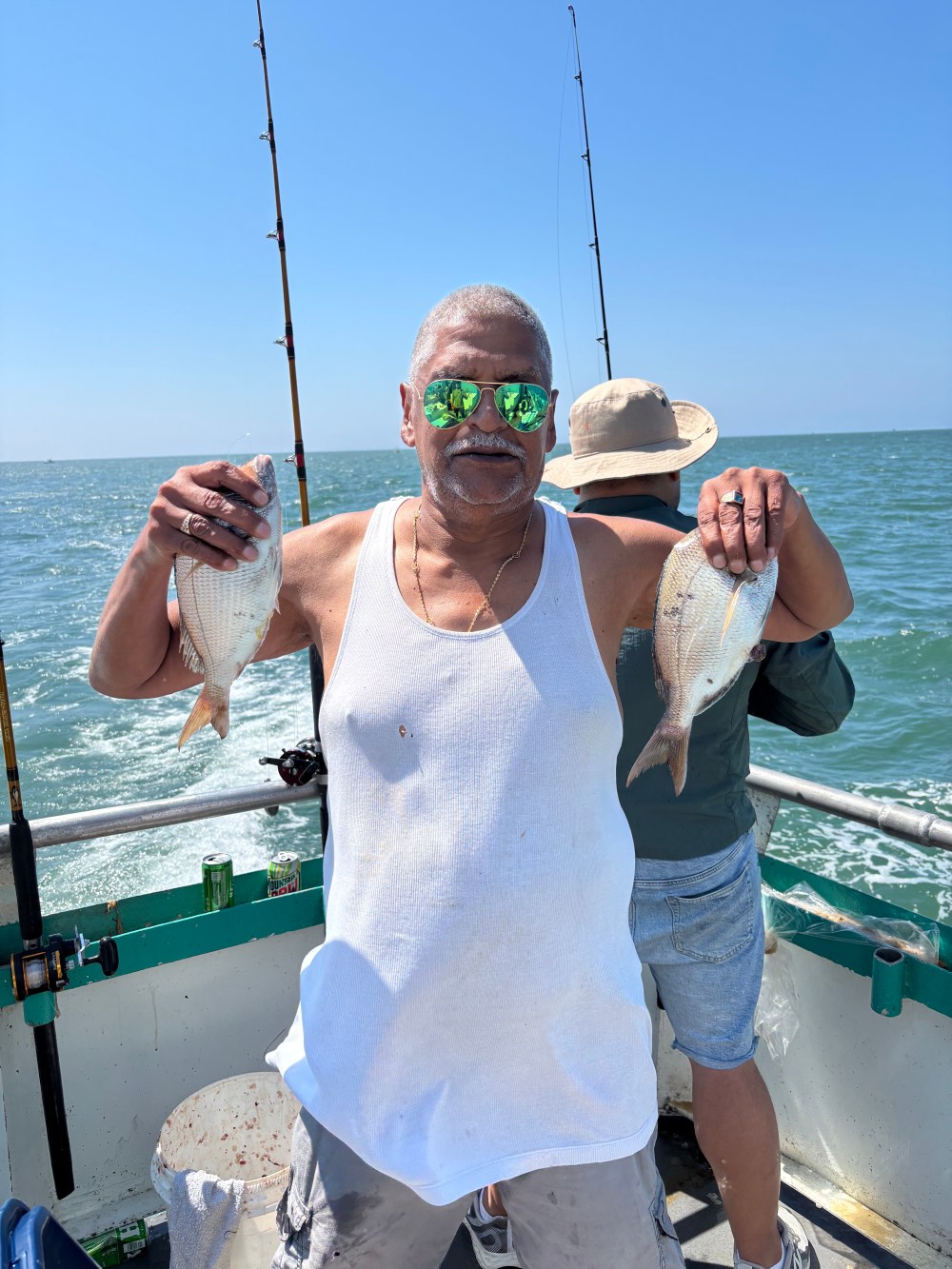 Man on boat holding two fish with ocean in background.