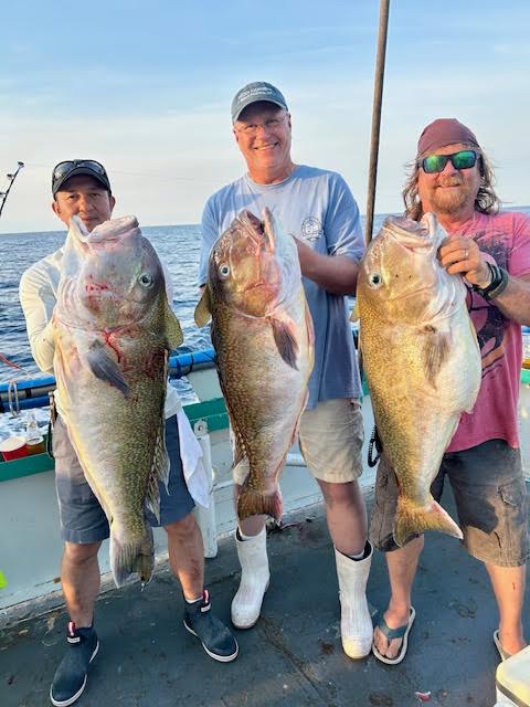 Three men on a boat holding large fish, smiling at the camera.
