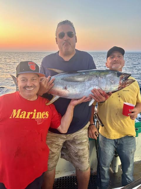 Three men on a boat holding a large fish at sunset.