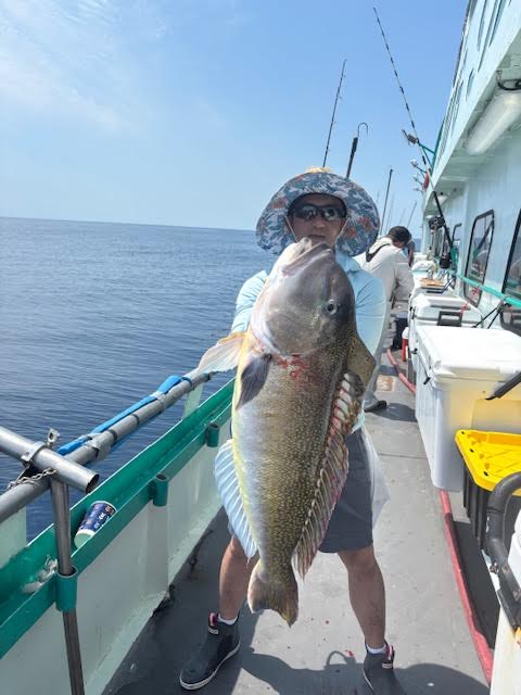 Person holding a large fish on a boat with ocean in the background.