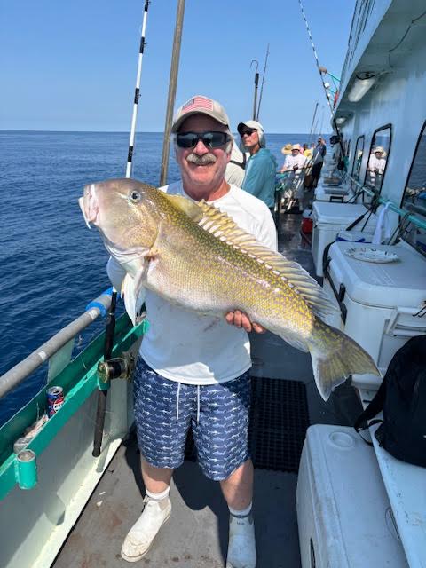 Man holding large fish on boat deck, ocean in background.