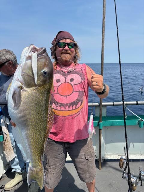 Man in a pink shirt holding a large fish on a boat.