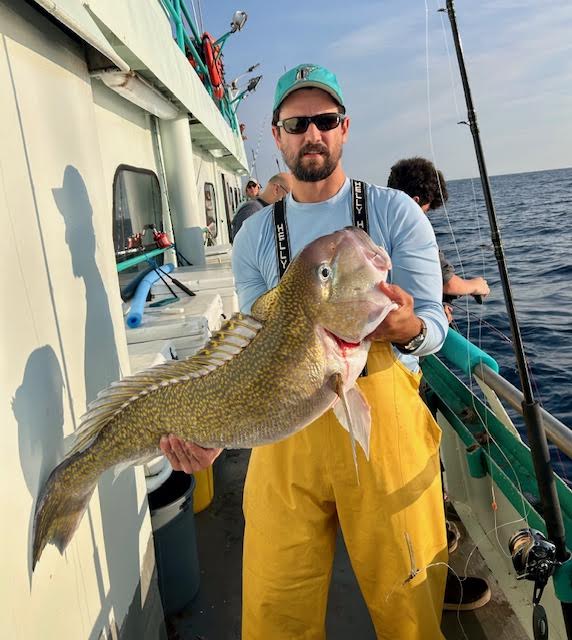 Man in yellow overalls holding a large fish on a boat.
