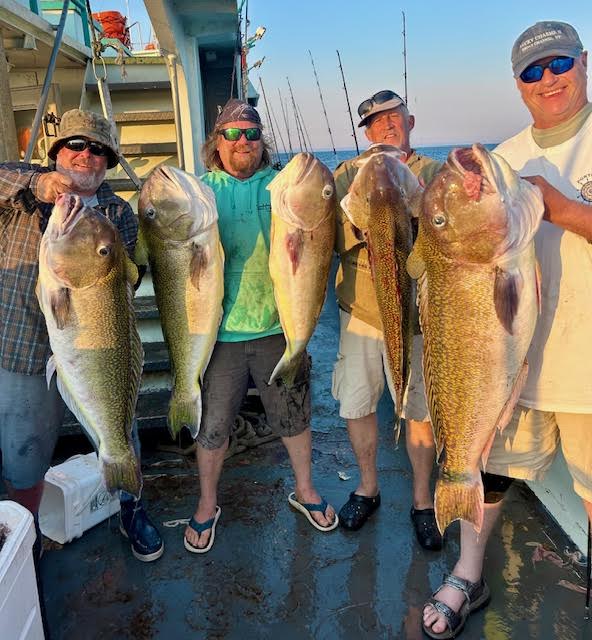 Four men on boat holding large fish, smiling.