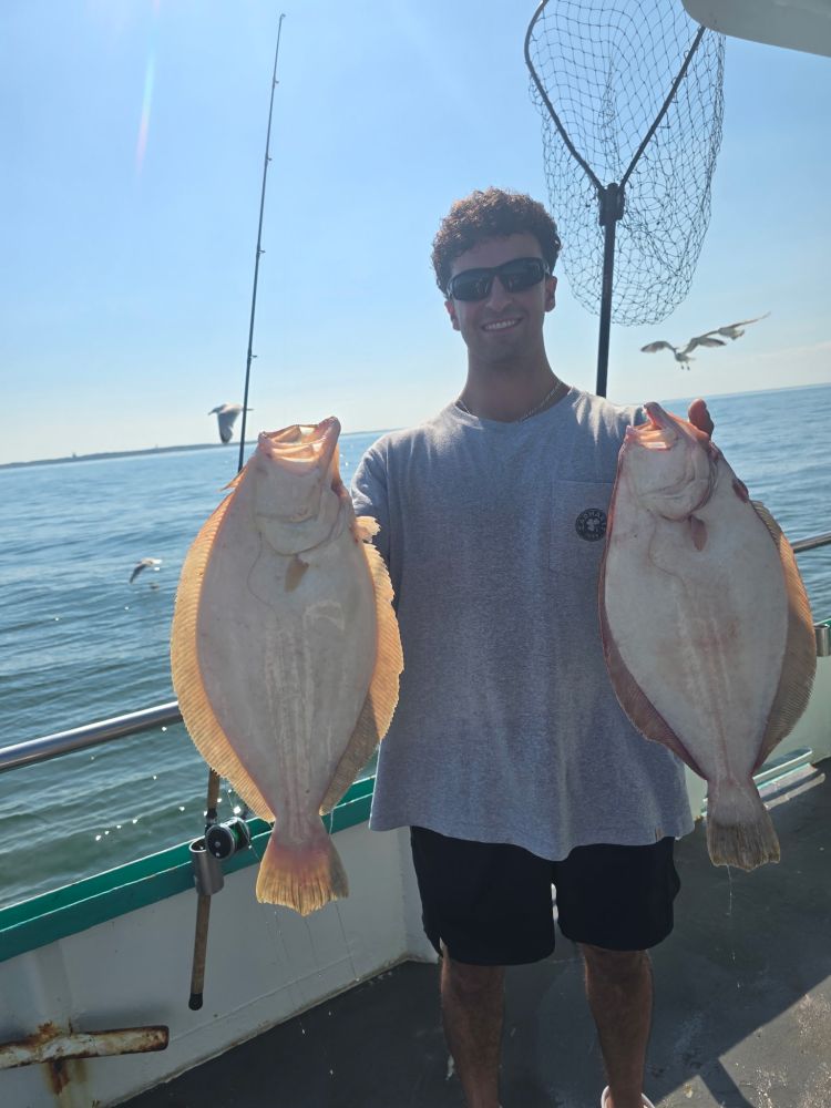 Man holding two large fish on a boat with ocean in background.