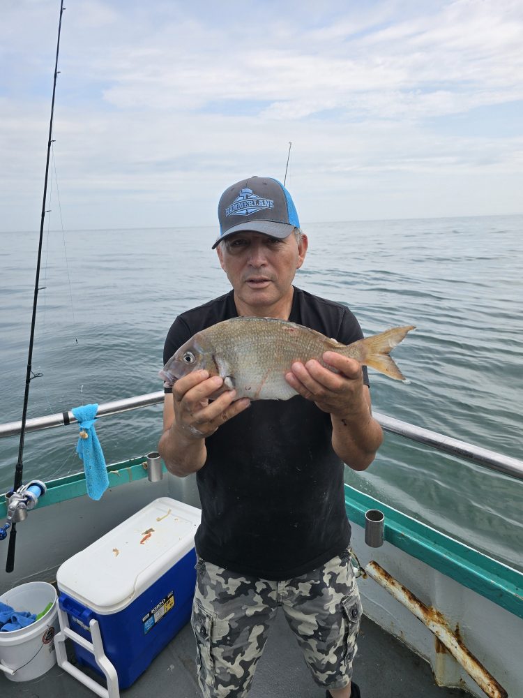 Person on boat holding a fish, with a cooler and fishing gear visible.