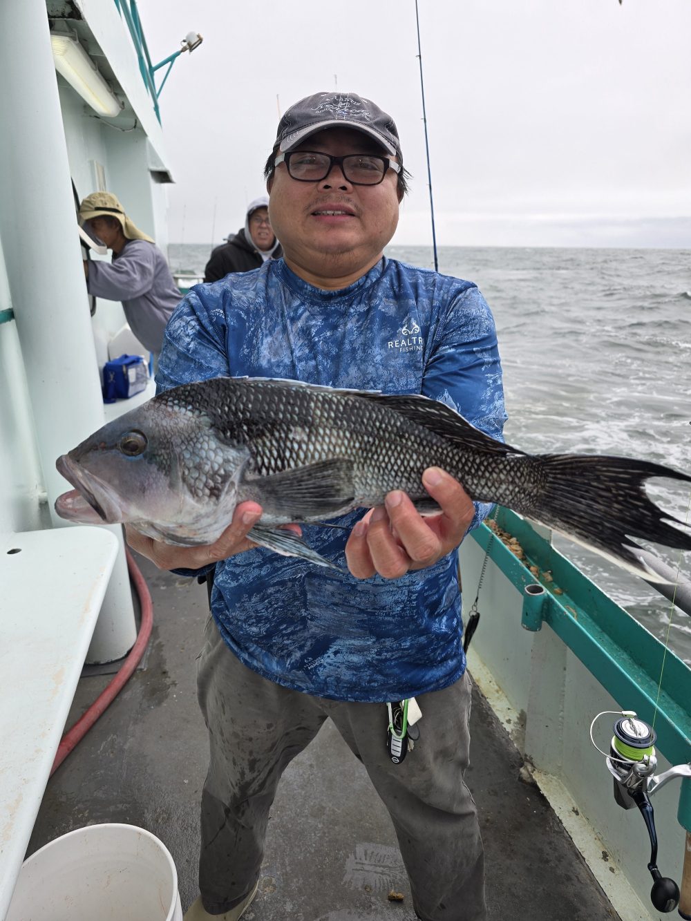 Person on a boat holding a large fish, wearing a blue shirt and cap.