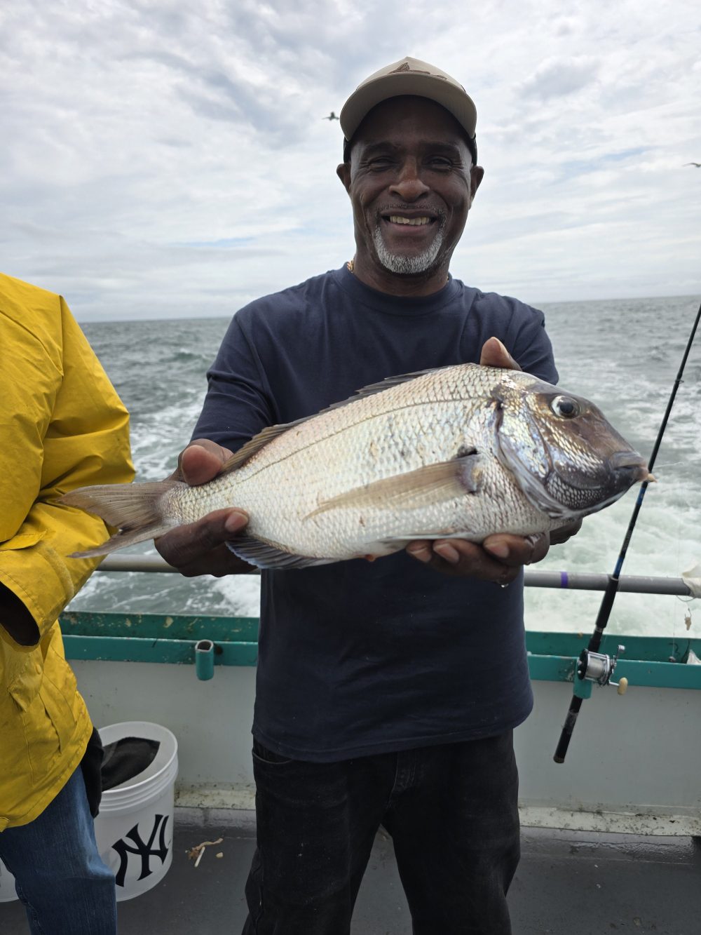 Man on a boat holding a large fish, smiling at the camera.