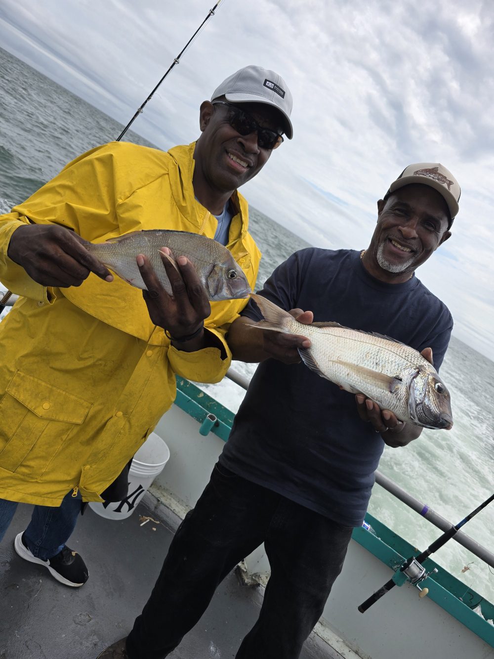 Two men on a boat holding fish, smiling at the camera.