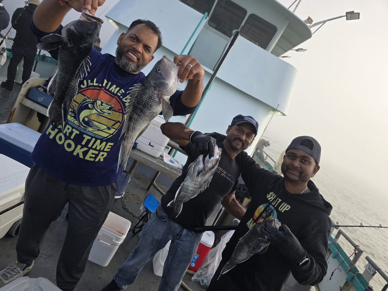 Three people on a boat holding fish, with fishing gear in the background.