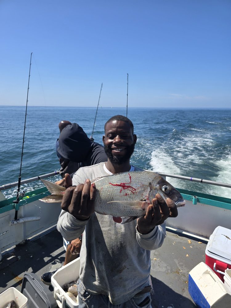 Person proudly holding a fish on a boat, with ocean visible in the background.