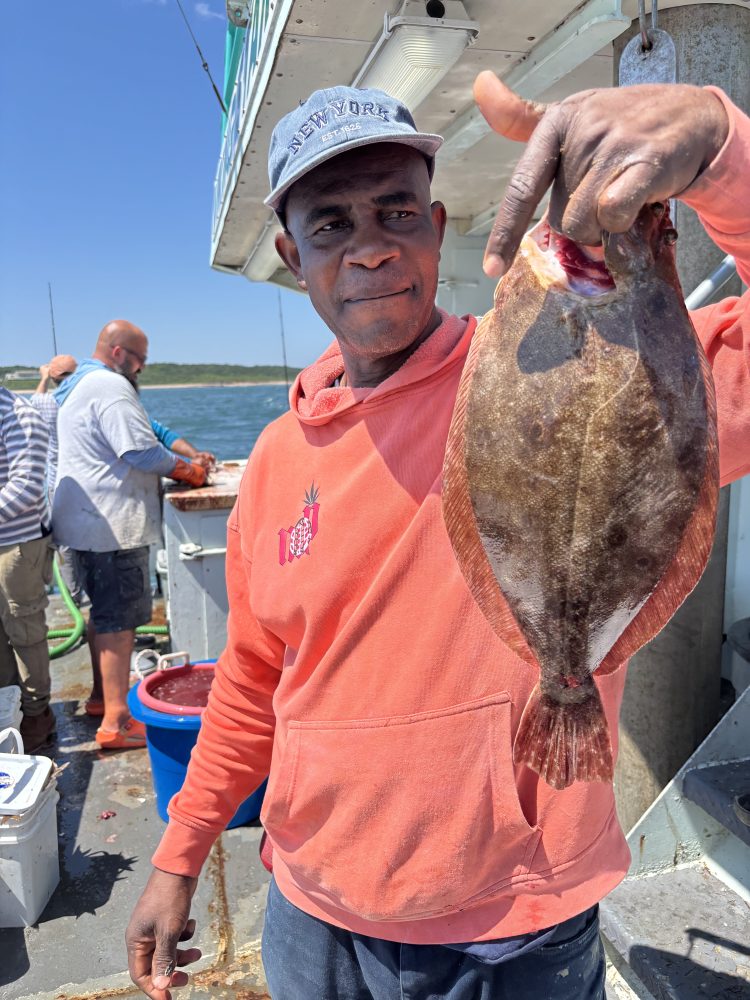 Man in orange hoodie holding a fish on a boat with others in the background.