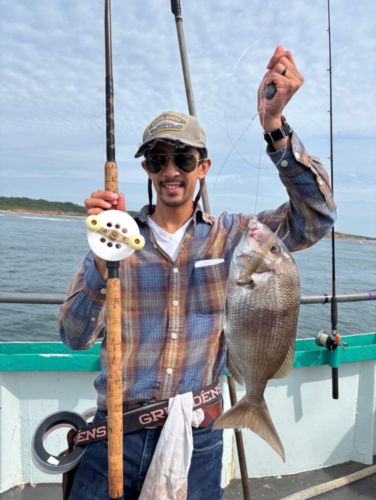 Man smiling, holding a fishing rod and a fish on a boat.