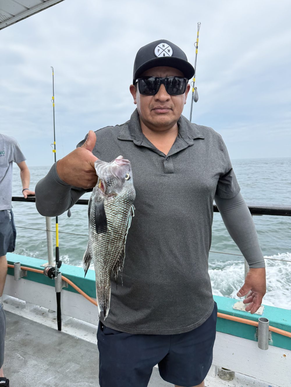 Man holding fish on a boat deck, wearing sunglasses and a hat.