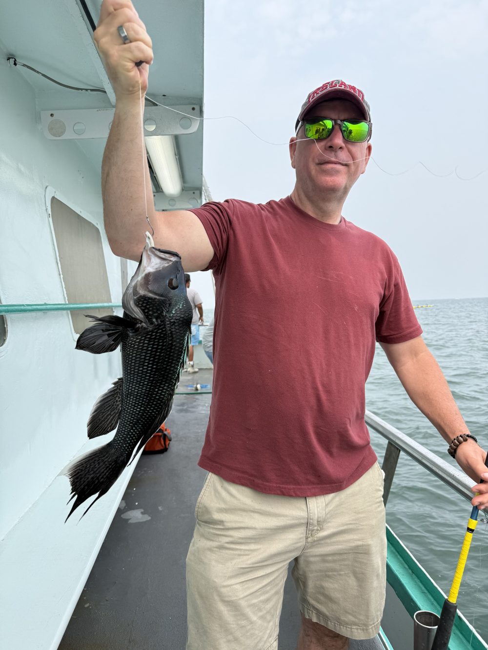 Person in red shirt holding caught fish on a boat.