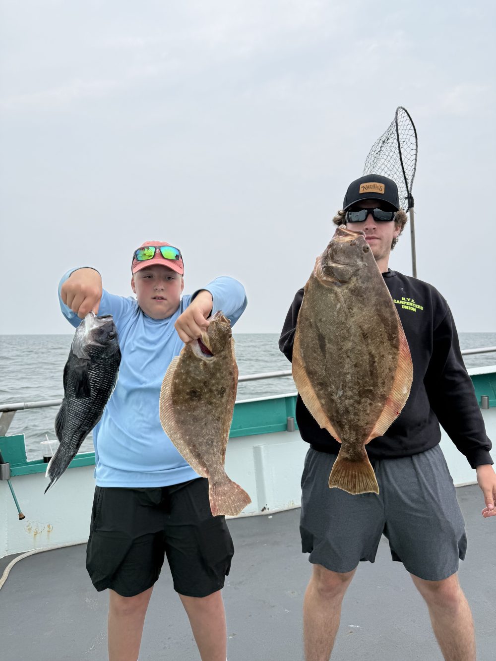 Two people on a boat holding fish, including a large flatfish.
