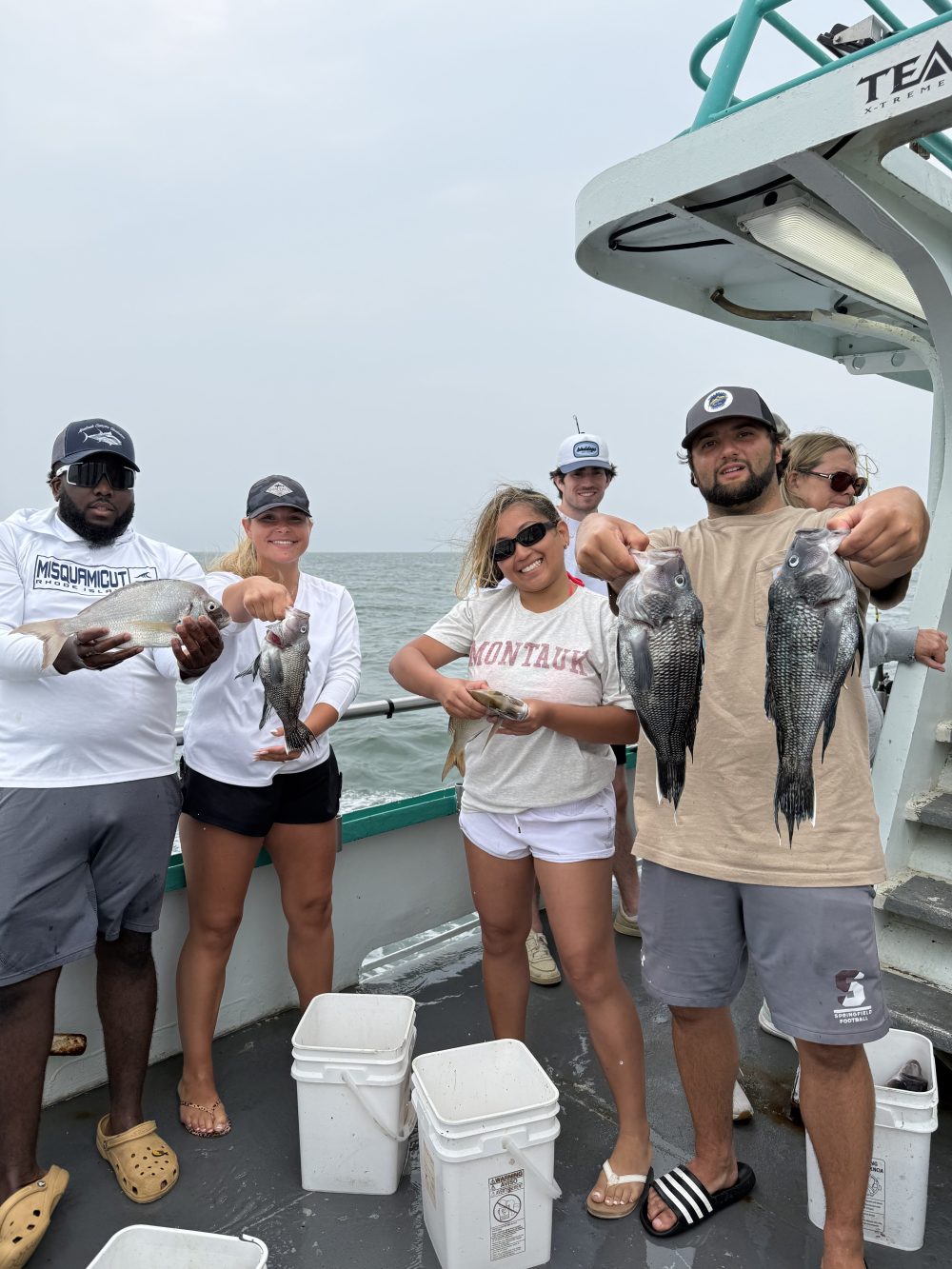 Group of people on a boat holding fish, smiling at the camera.