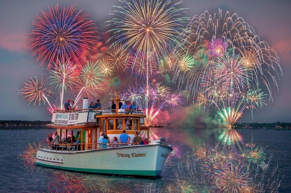 Boat on water with colorful fireworks exploding in the sky.