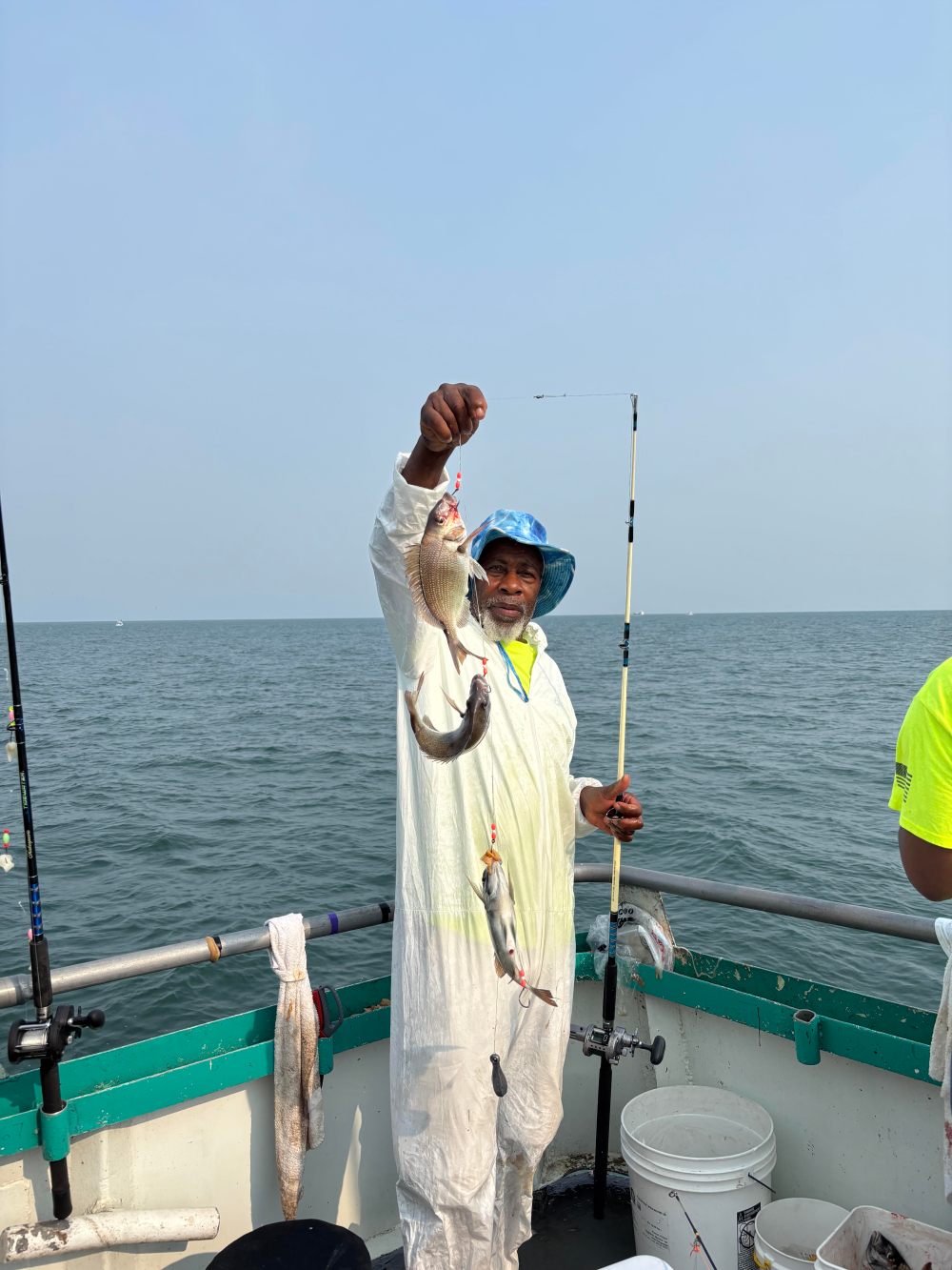 Person in white suit holds up caught fish on a boat at sea.