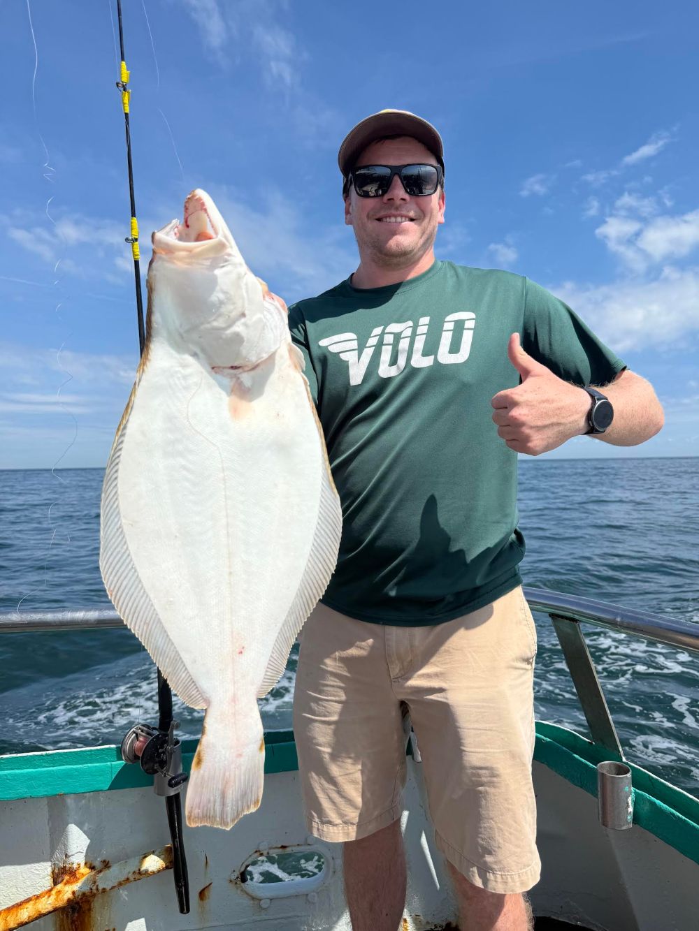 Person on a boat holding a large fish and giving a thumbs-up.