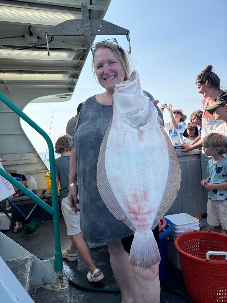 Person holding a large fish on a boat with people in the background.