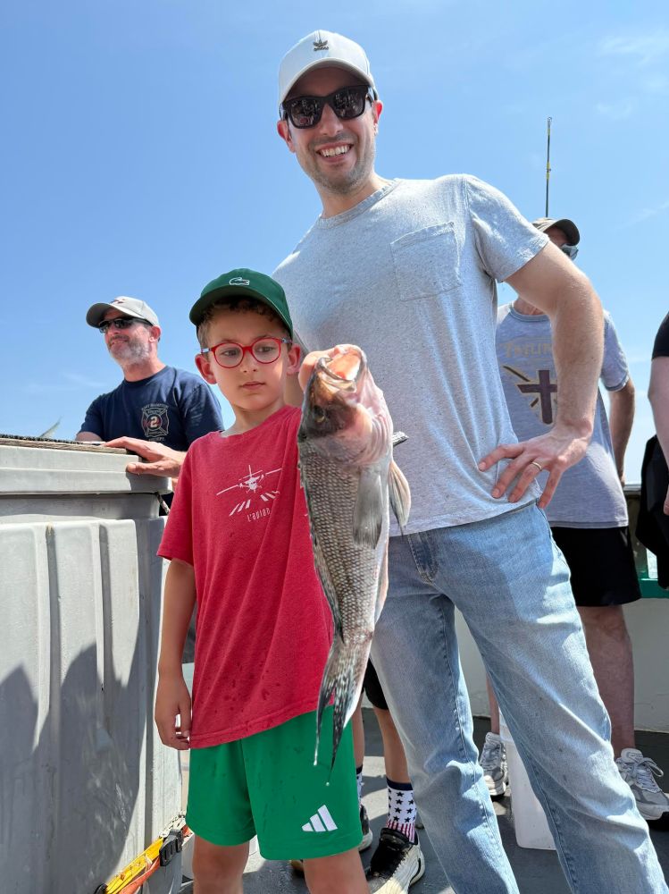 Man and boy on boat holding a large fish, others in background.