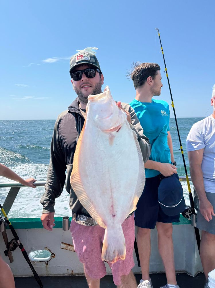 Person holding a large flat fish on a boat with the ocean in the background.