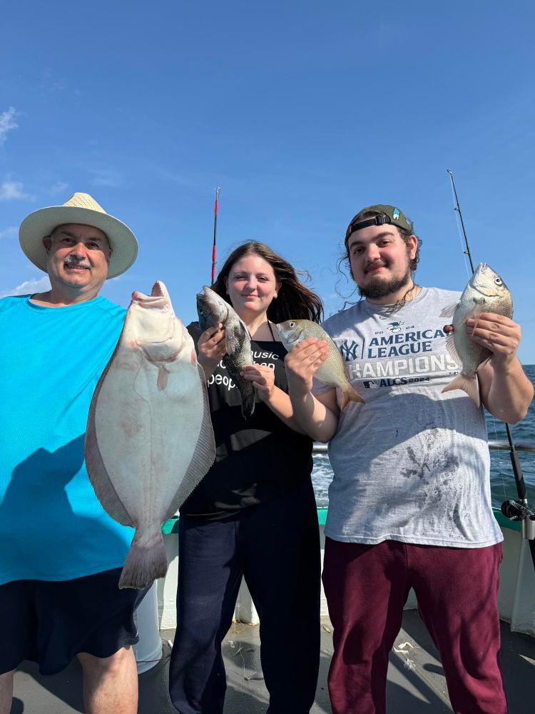 Three people holding fish on a boat under a clear blue sky.