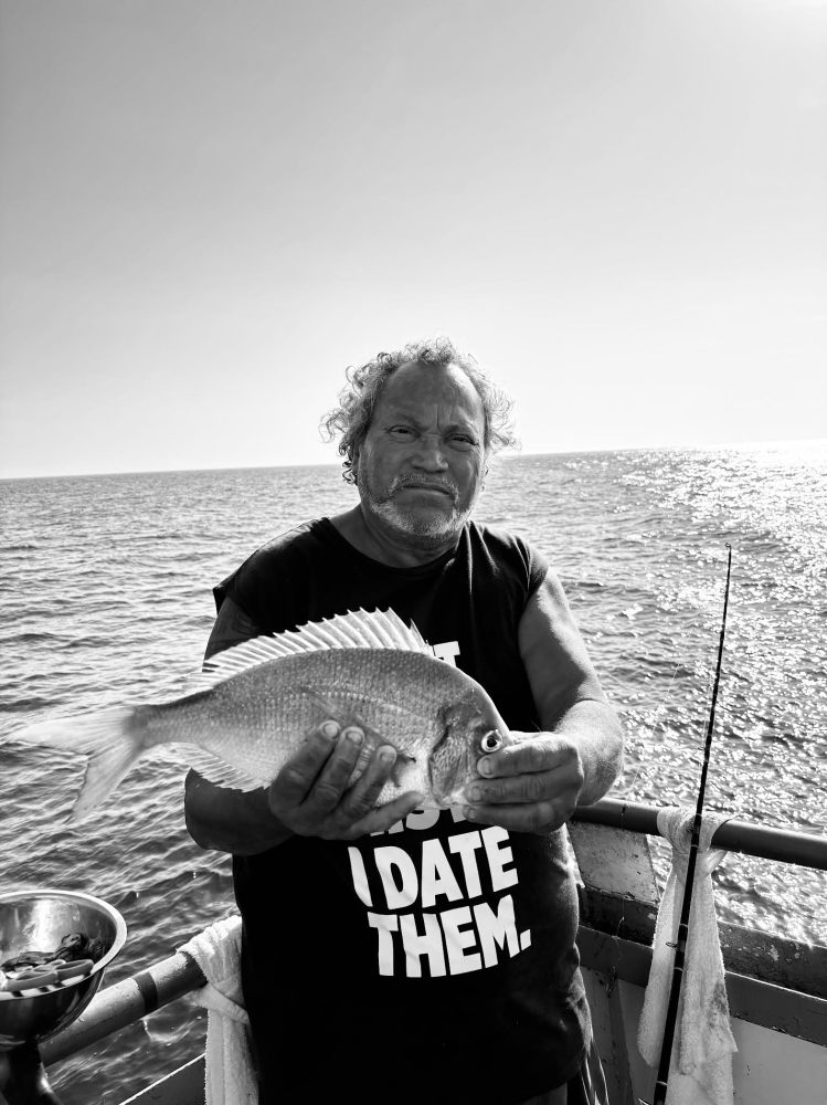 Man holding a fish on a boat with ocean in the background.