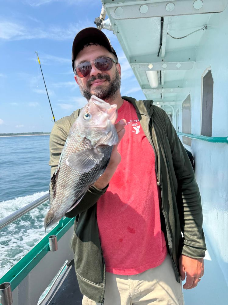Person holding a large fish on a boat deck, wearing a red shirt and sunglasses.