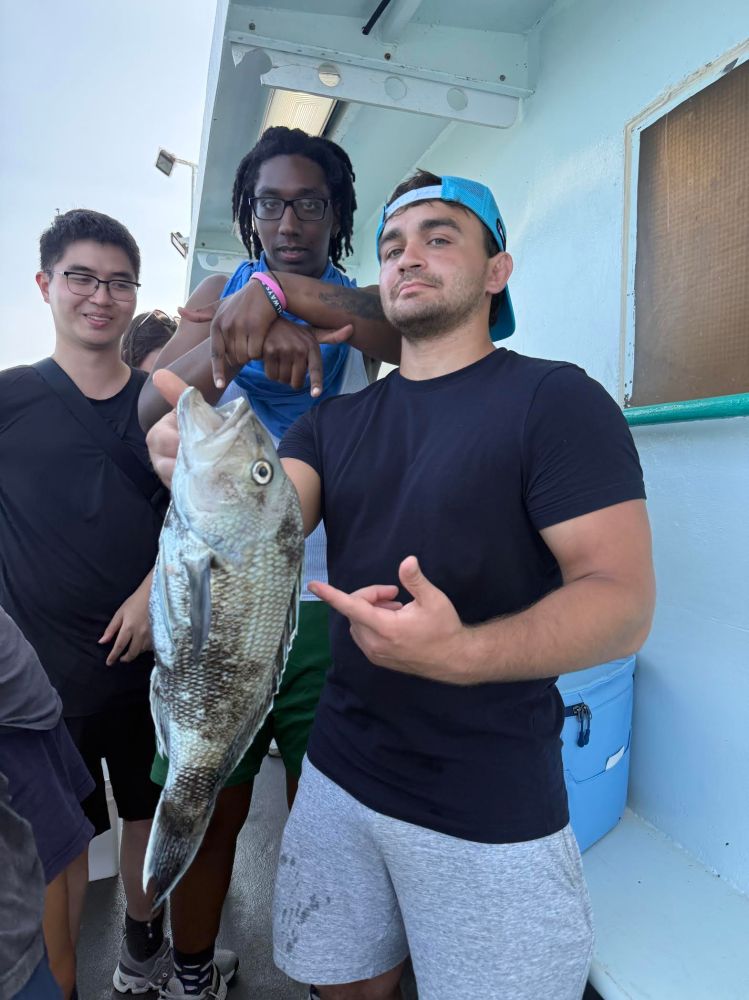 Three people on a boat; one holding a fish up close.