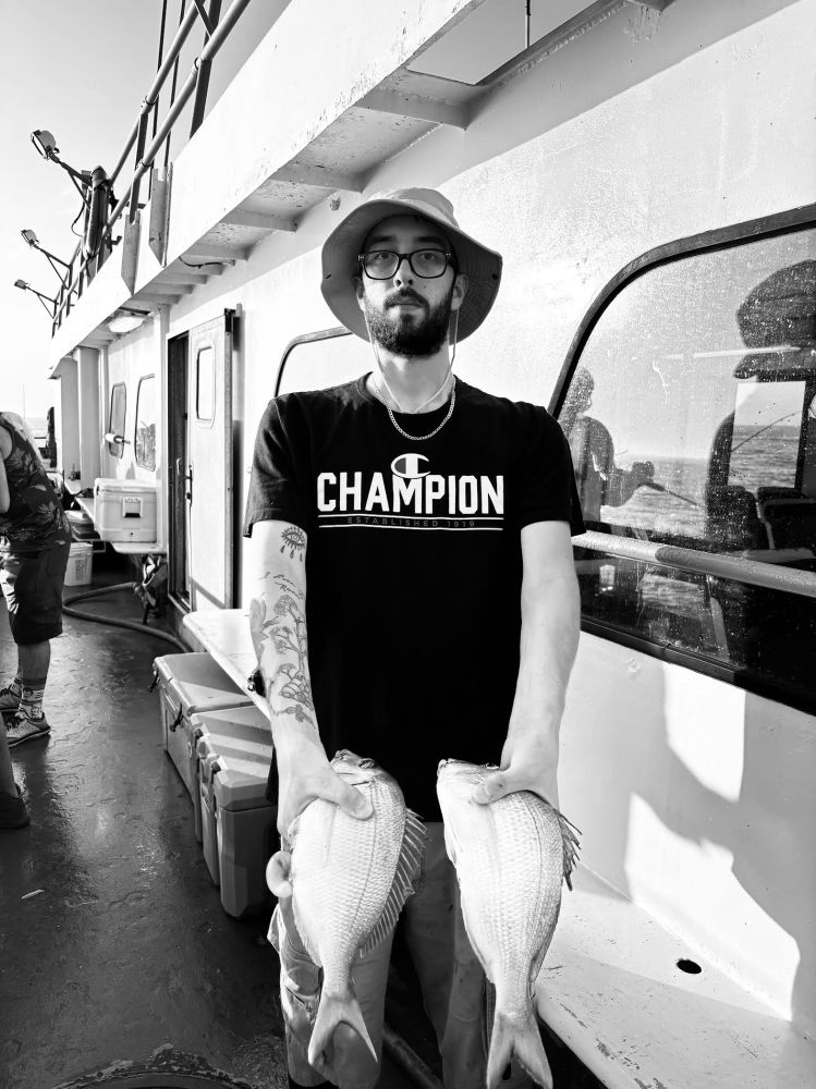 Man on a boat holding two fish, wearing a hat and glasses.