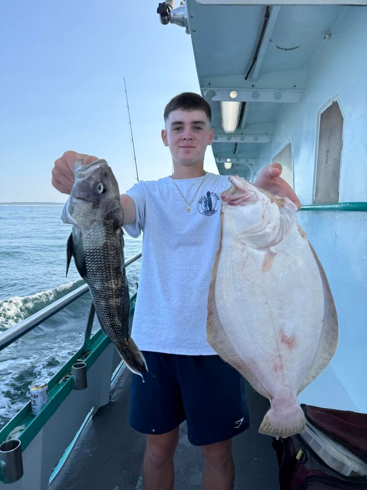 Person on a boat holding a black fish and a flatfish with both hands.