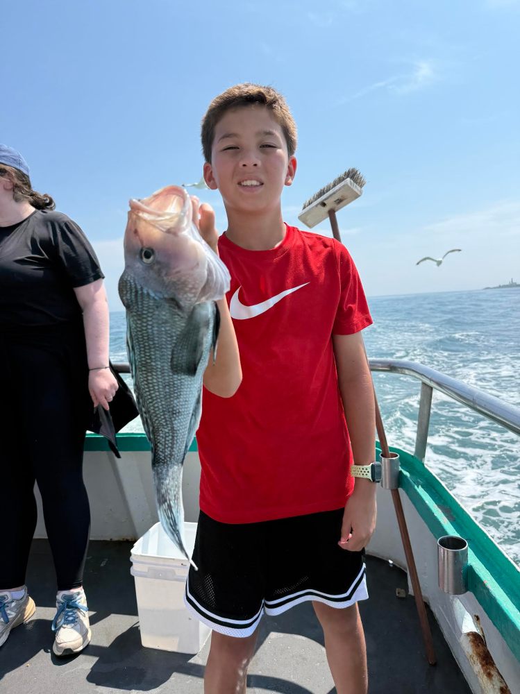 Child in a red shirt holding a fish on a boat, with water and a bird in the background.