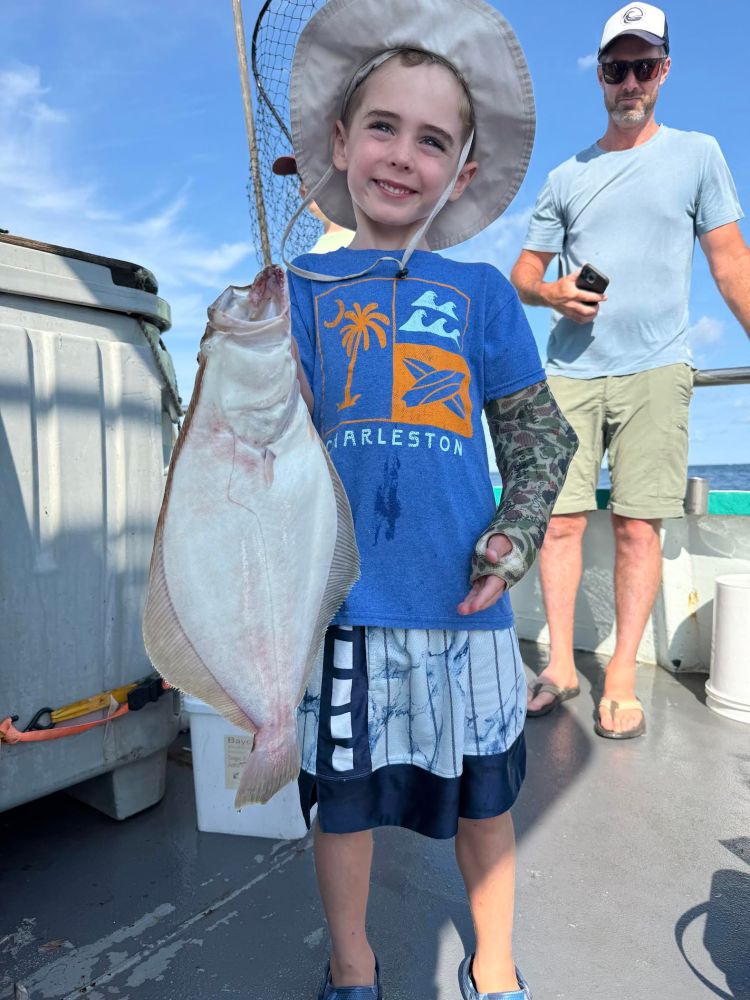 Boy holding a large fish on a boat, with a man in the background.