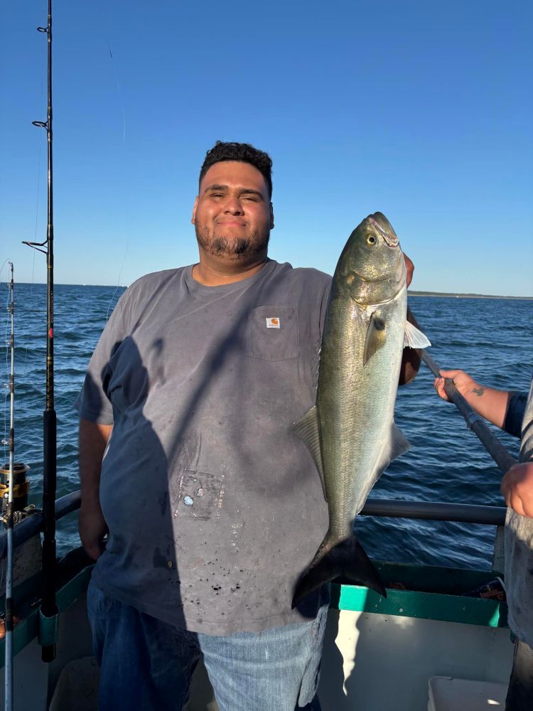 Man on boat holding a large fish with a fishing rod nearby.