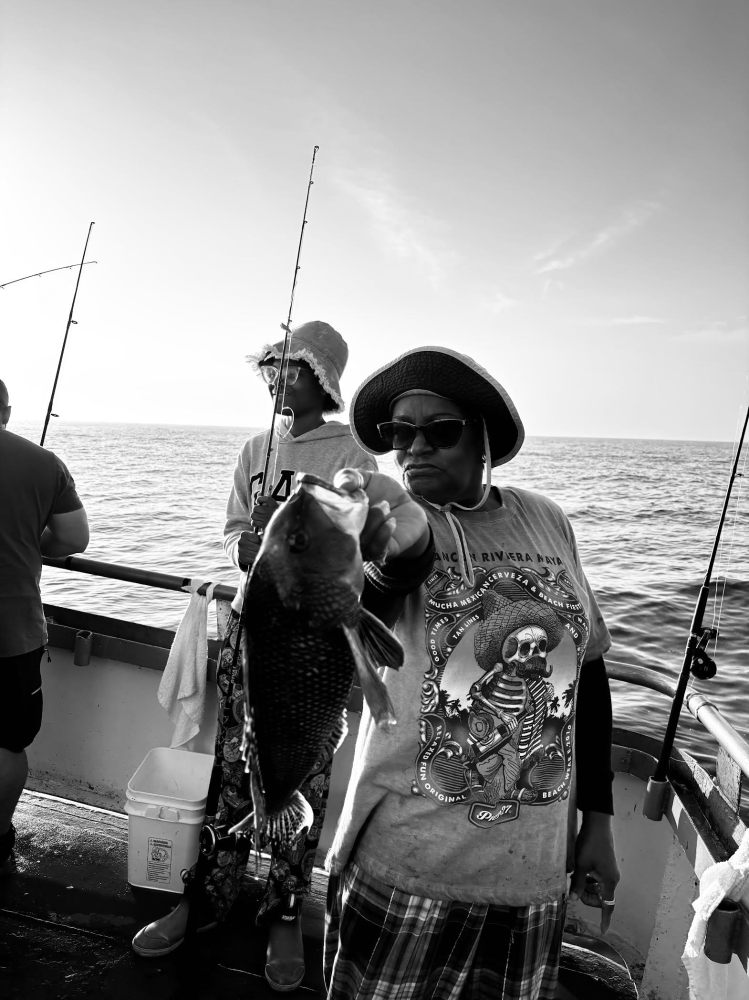 People fishing on a boat; person holds up a caught fish.