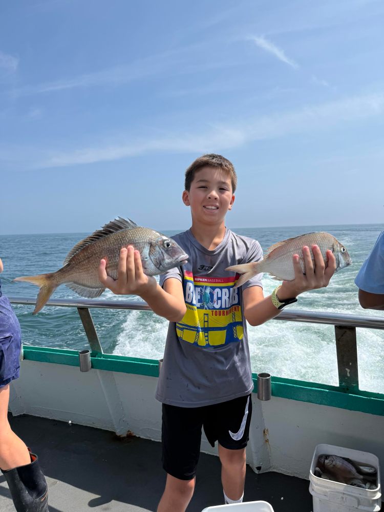 Boy holding two fish on a boat with ocean in the background.