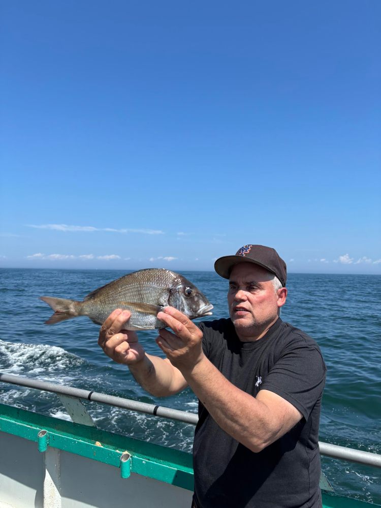 Man on boat holding a fish with ocean in background.
