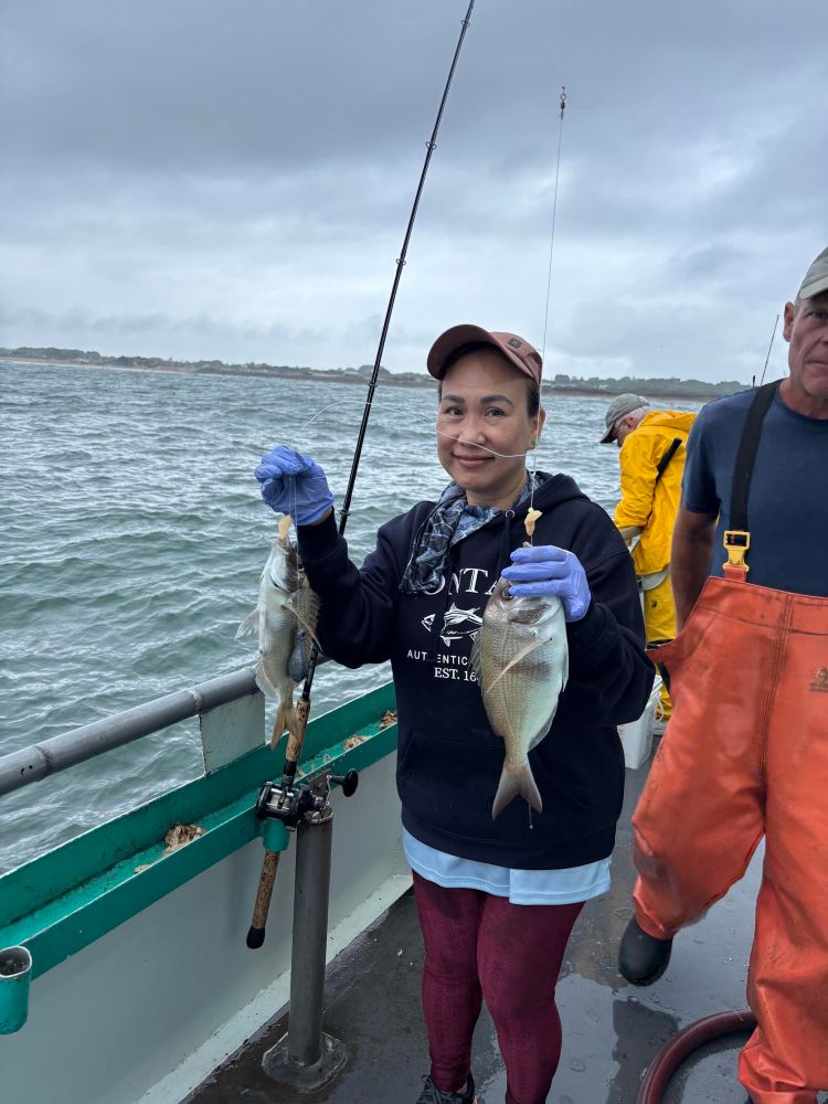 Person holding two fish on a boat with cloudy sky background.
