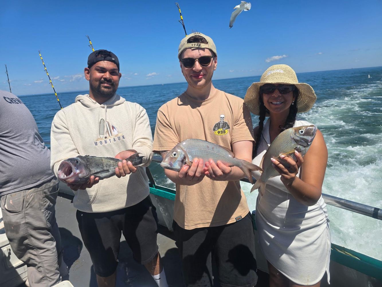 Three people on a boat holding fish, with the ocean in the background.