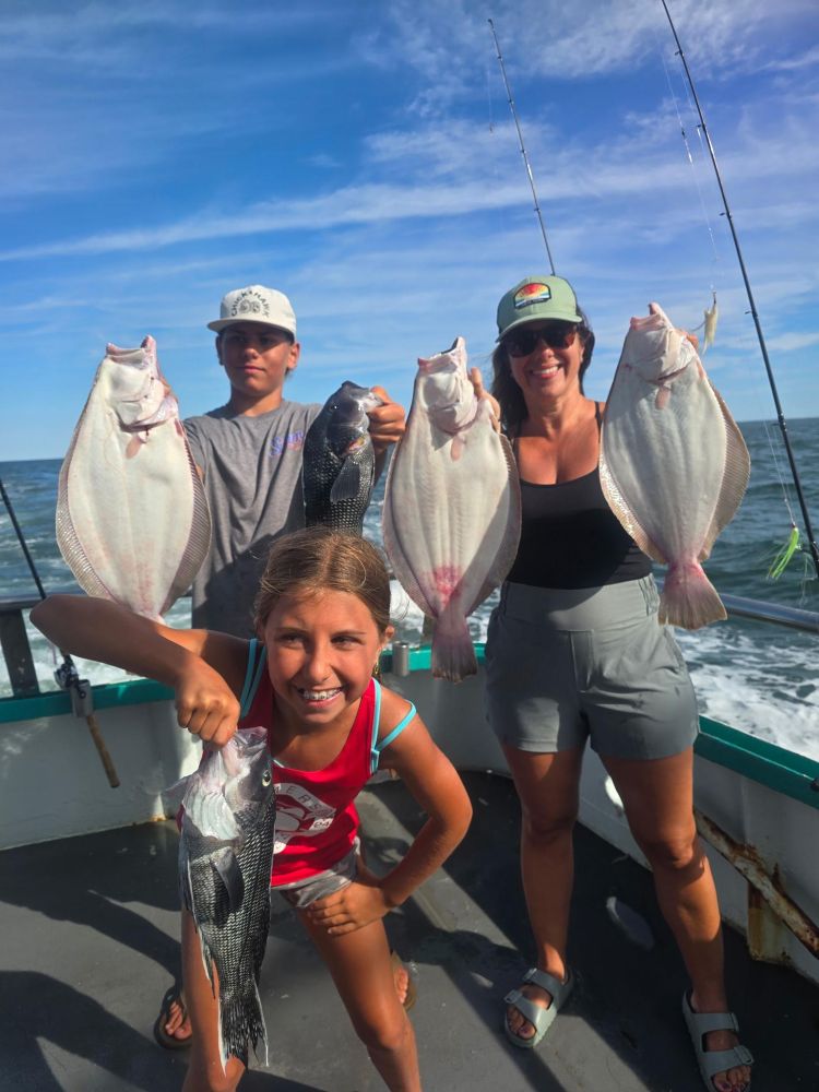 Three people on a boat holding fish they caught.