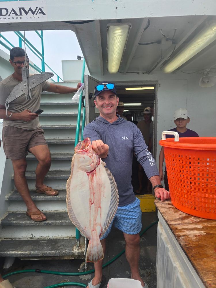 Man on boat holding a large flat fish with others nearby.