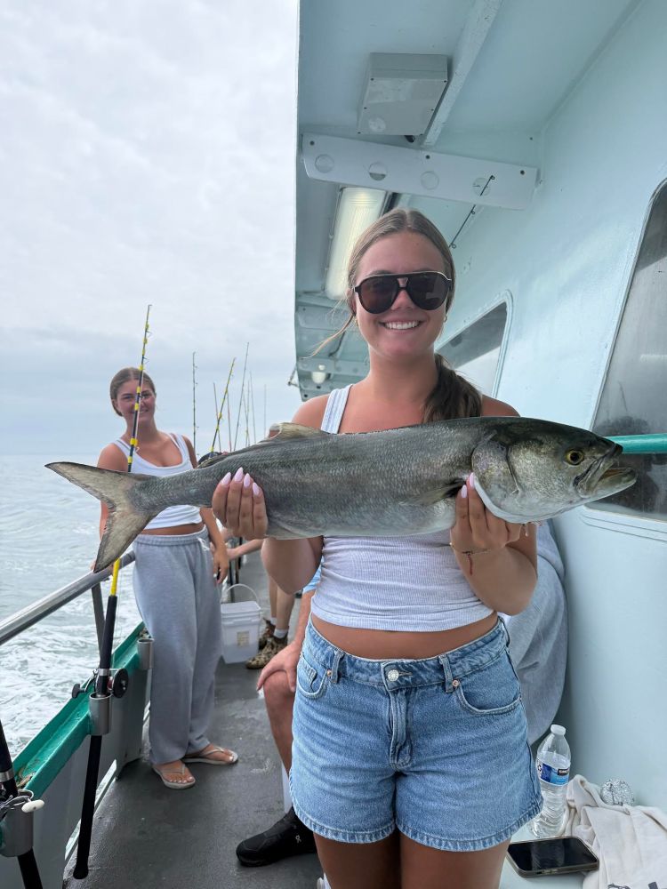 Smiling woman in sunglasses holding a large fish on a boat.