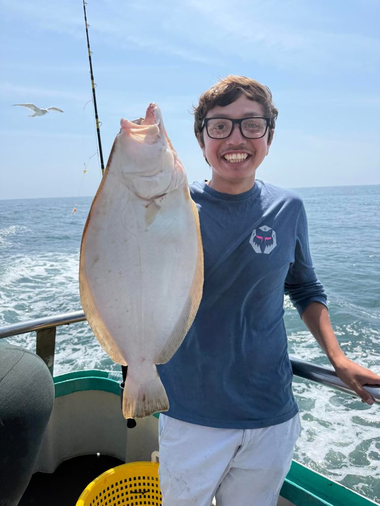 Person smiling on boat holding a large fish, with ocean and seagull in background.