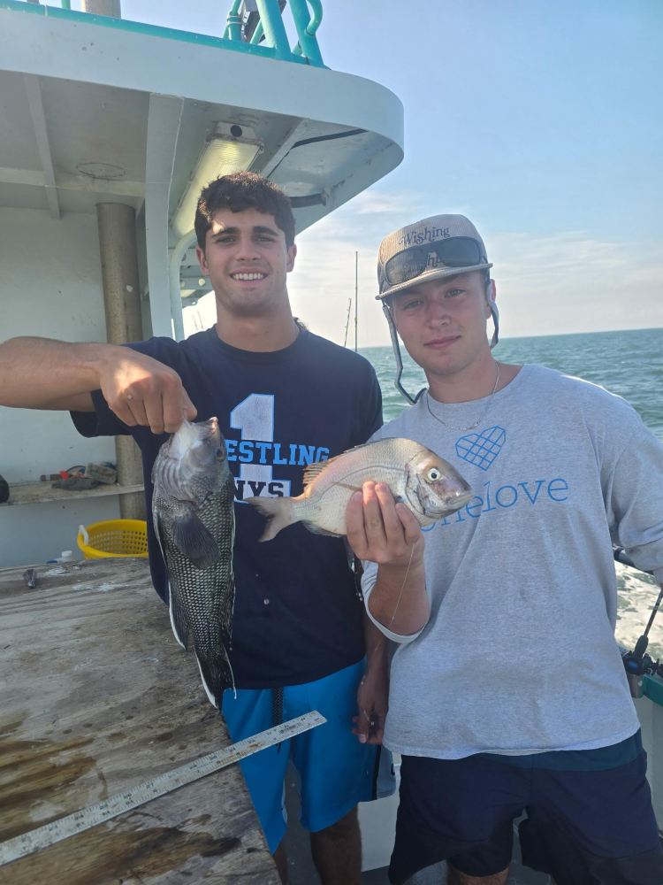 Two men on a boat holding freshly caught fish.