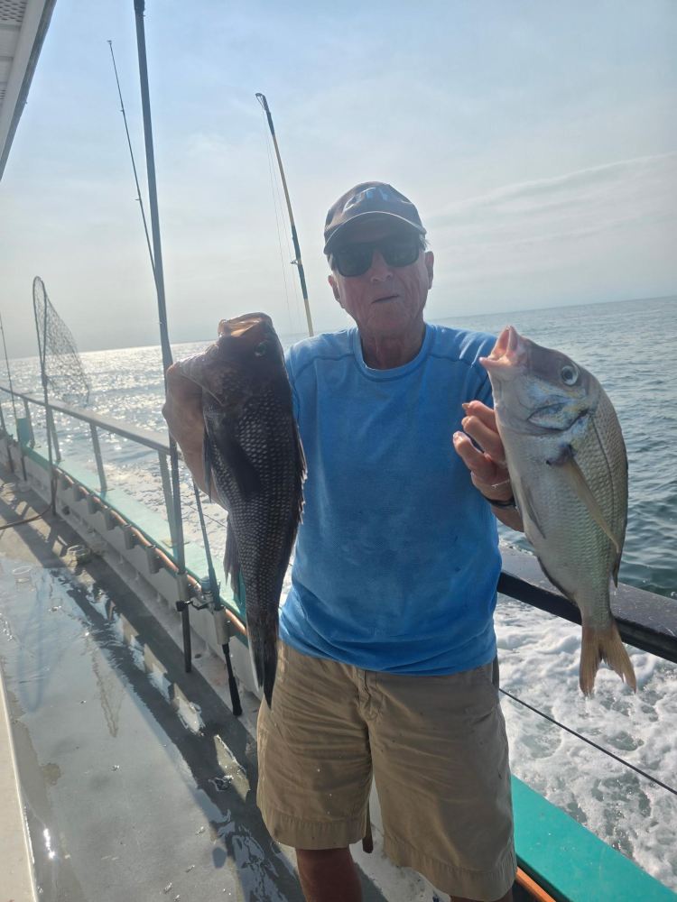 Man holding two fish on a boat at sea.