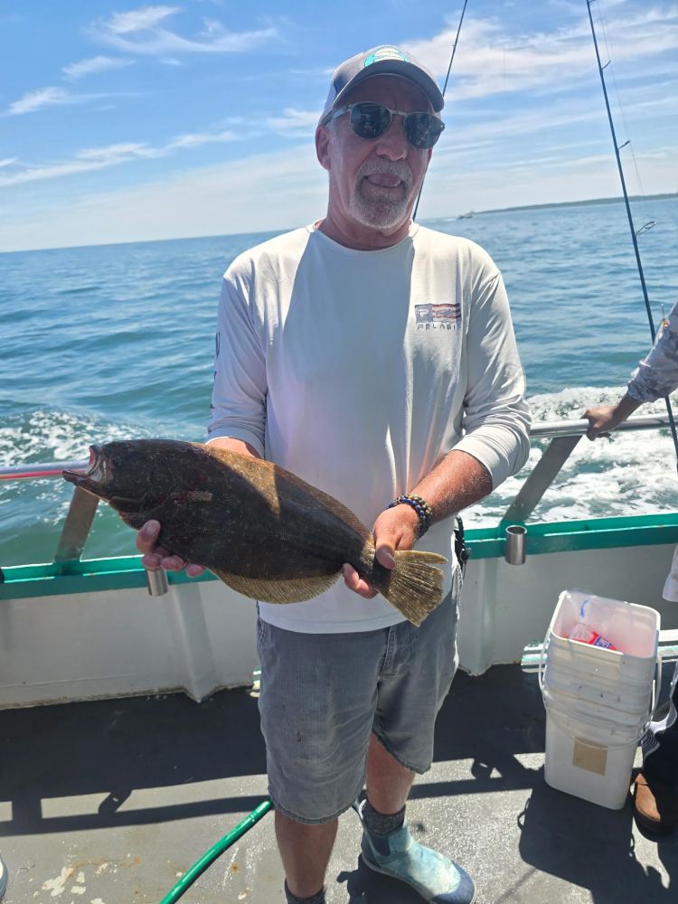 Man holding a fish on a boat under clear skies.
