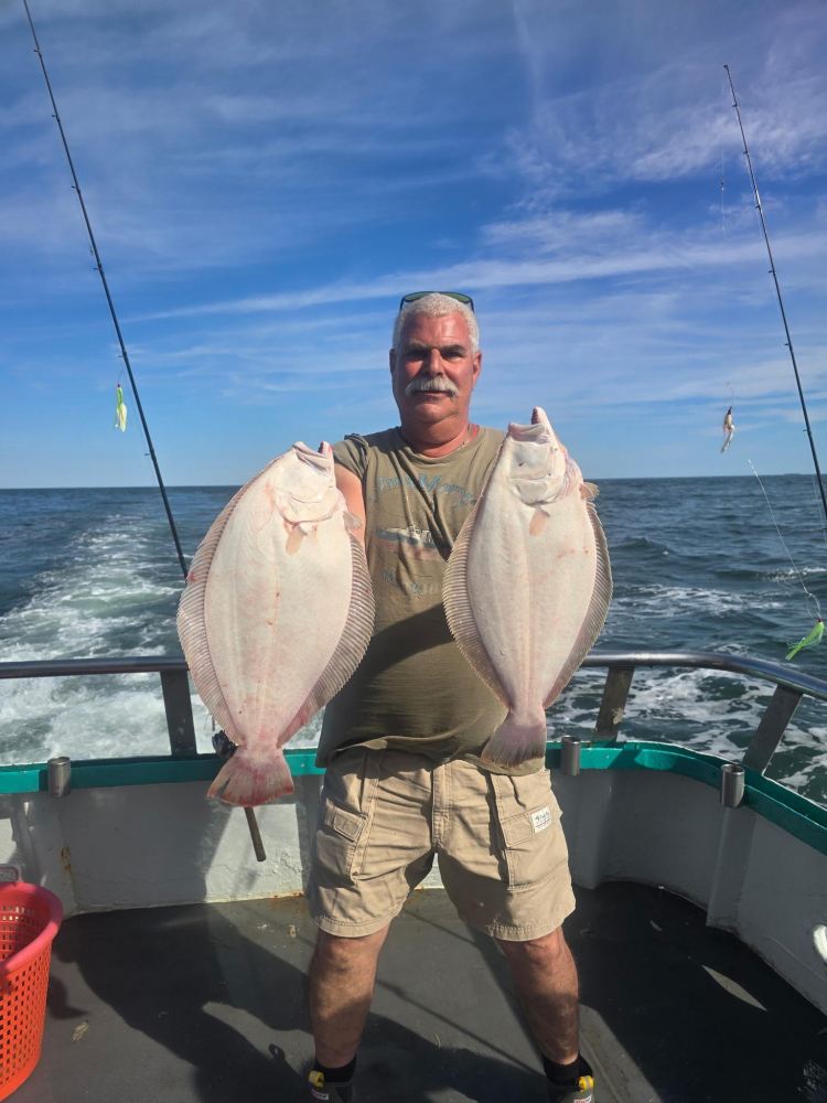 Man on boat holding two flat fish, ocean in background.